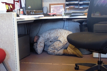 A Marine takes shelter beneath a desk in this image.
